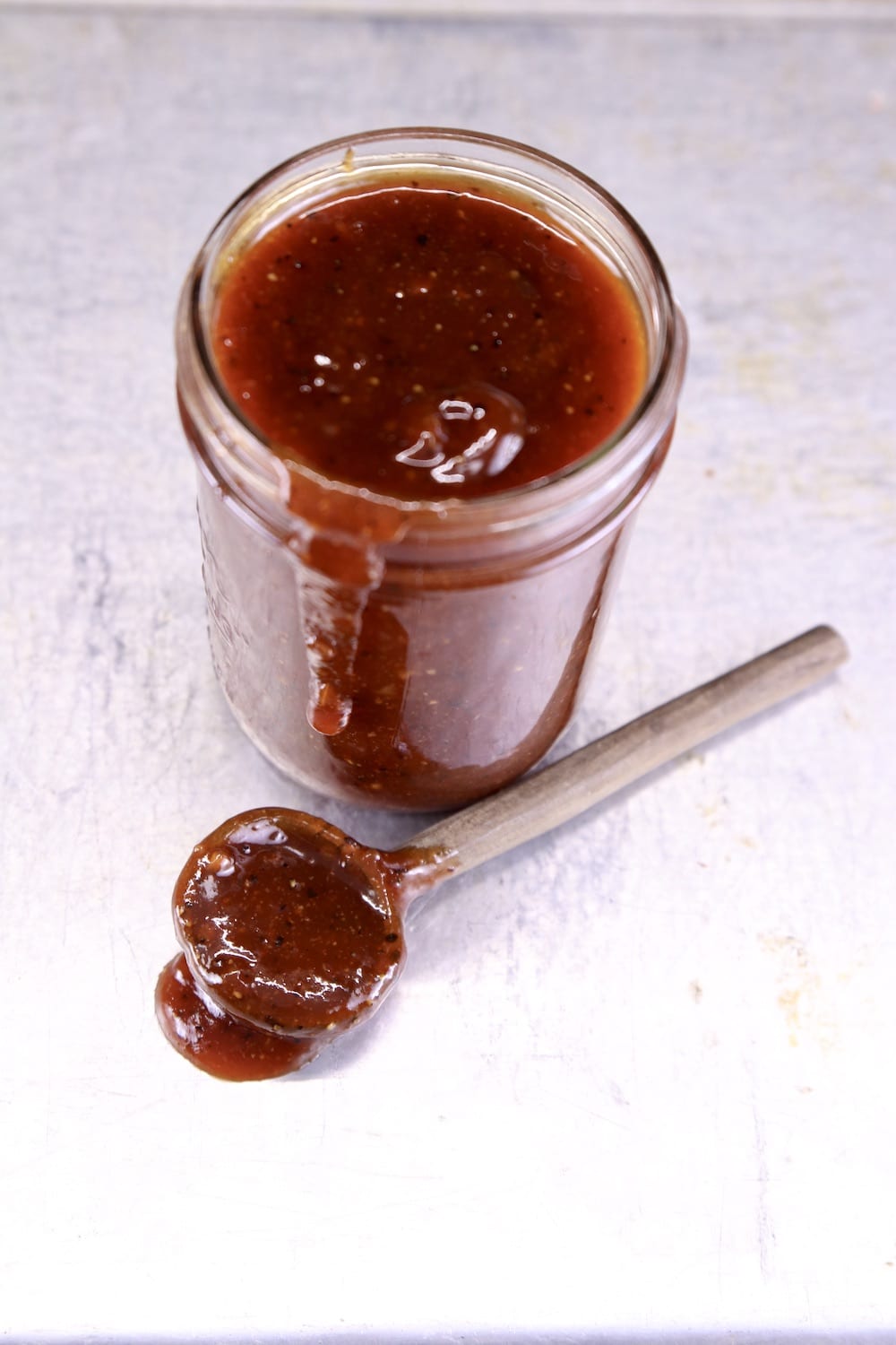 jar of bbq sauce with a spoon of sauce on the sheet pan