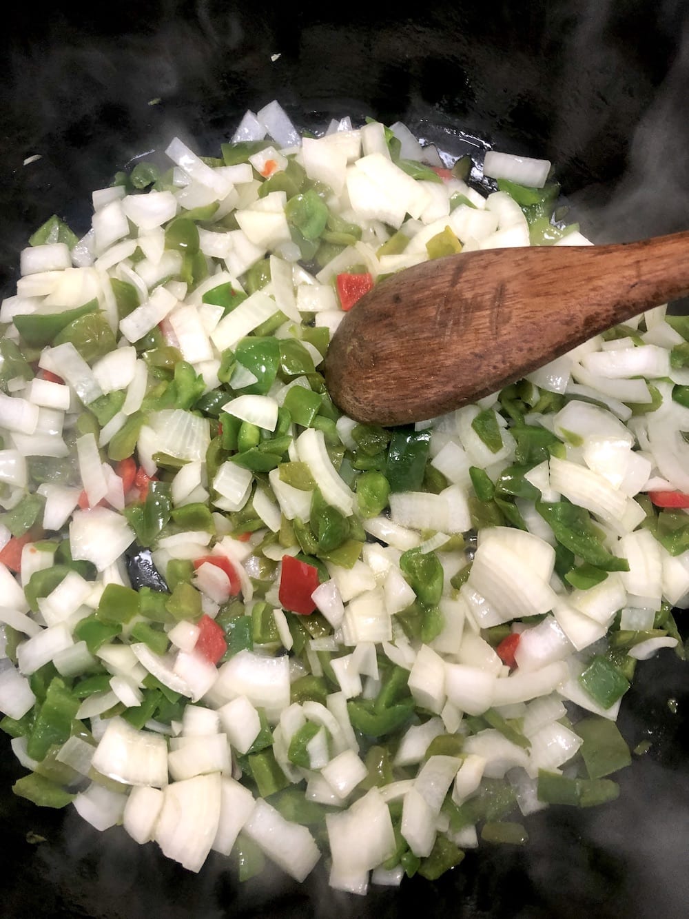 cast iron dutch oven with diced onions and peppers, with a wooden spoon