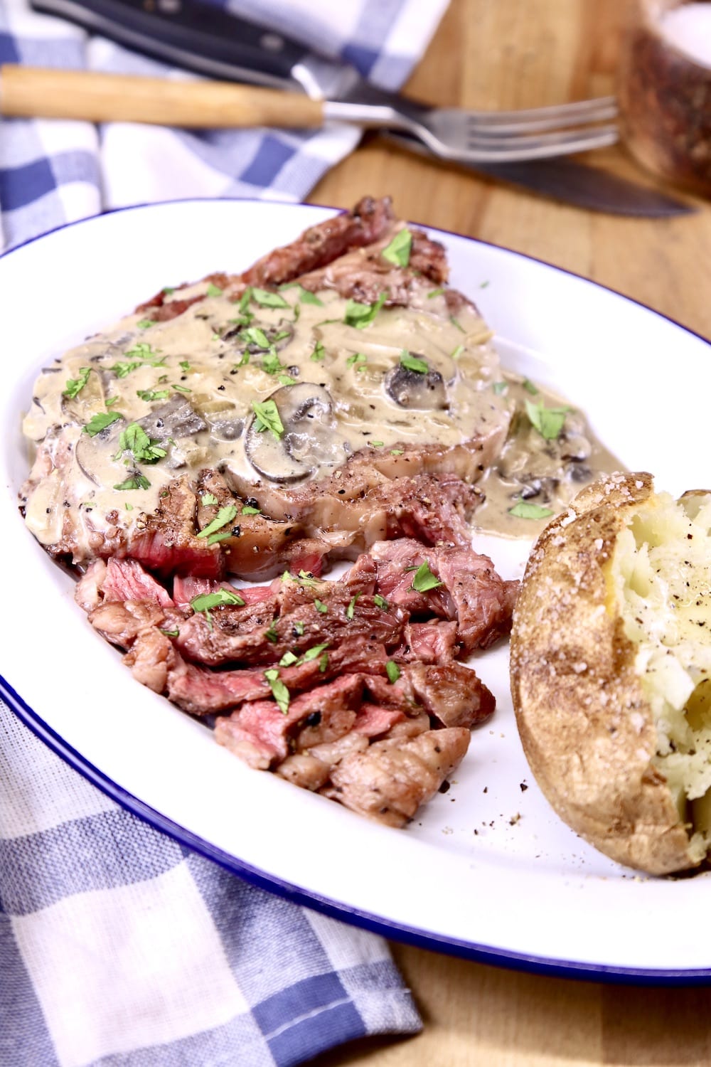 Grilled steak with mushroom cream sauce on a plate with a baked potato