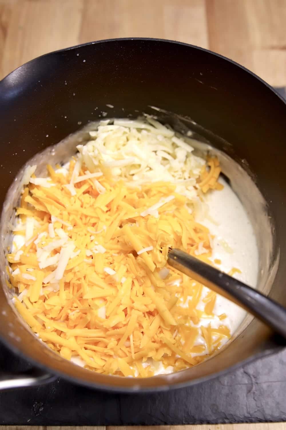 shredded cheese added to sauce in a pan with whisk