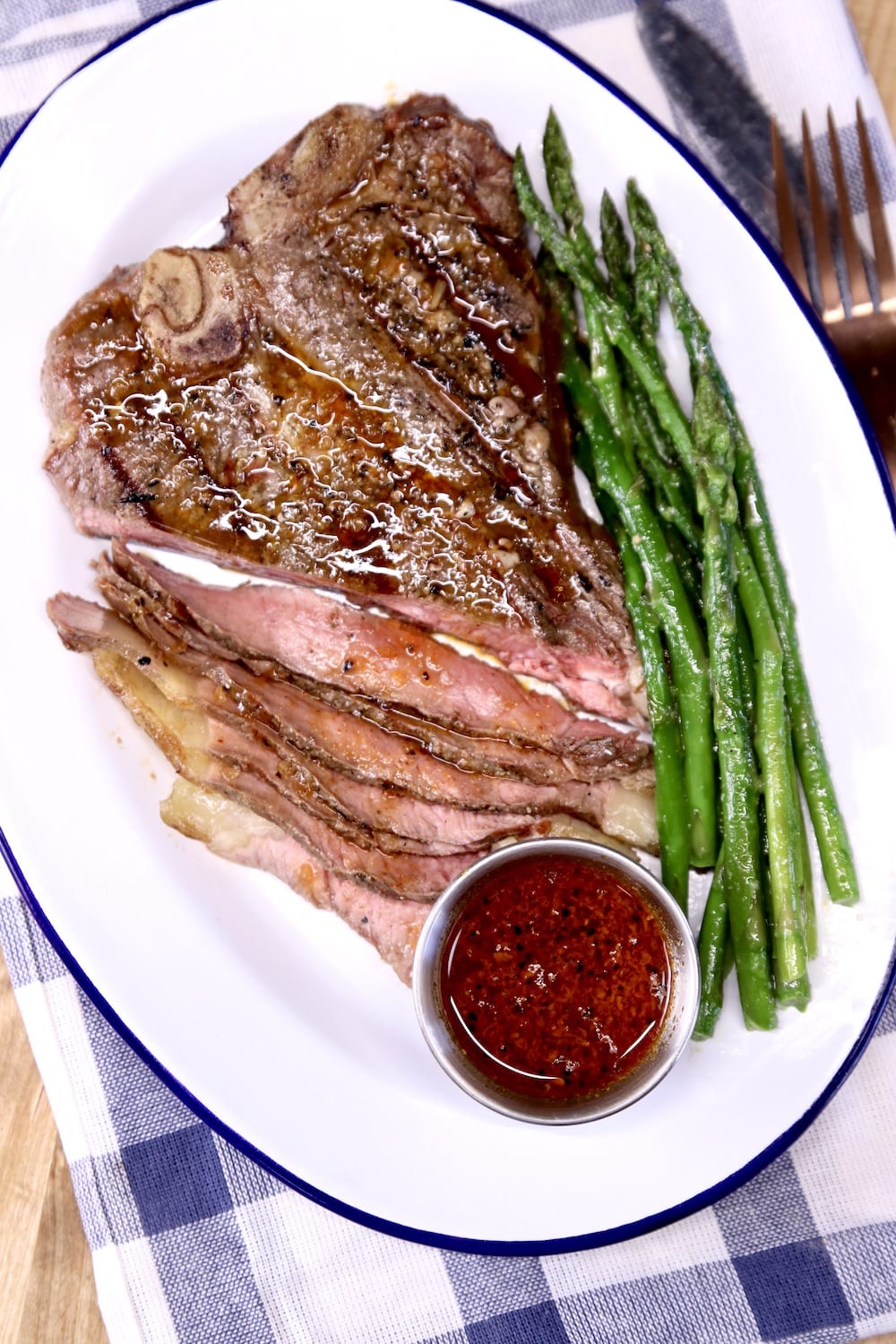 T-Bone Steak on a plate with asparagus and cup of sauce