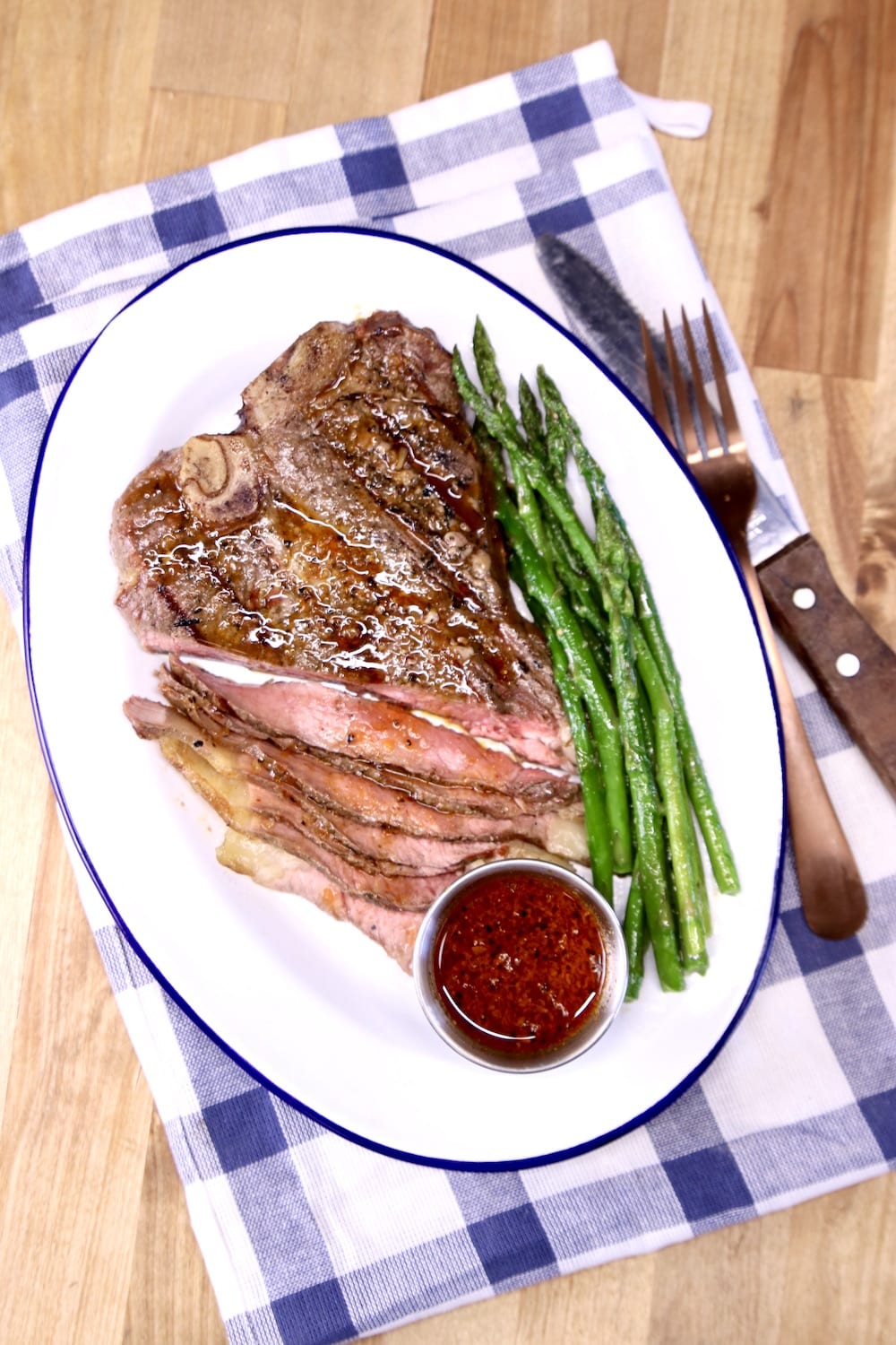 Plate of steak and asparagus with cup of sauce. Knife, fork and napkin