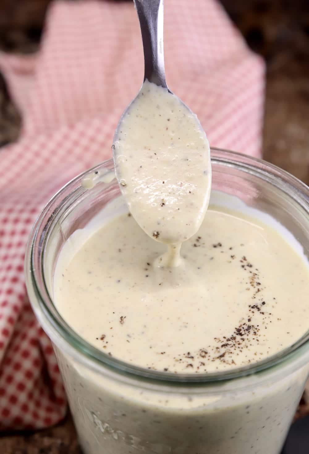 White BBQ Sauce with a spoon dipping from the jar over a red check napkin