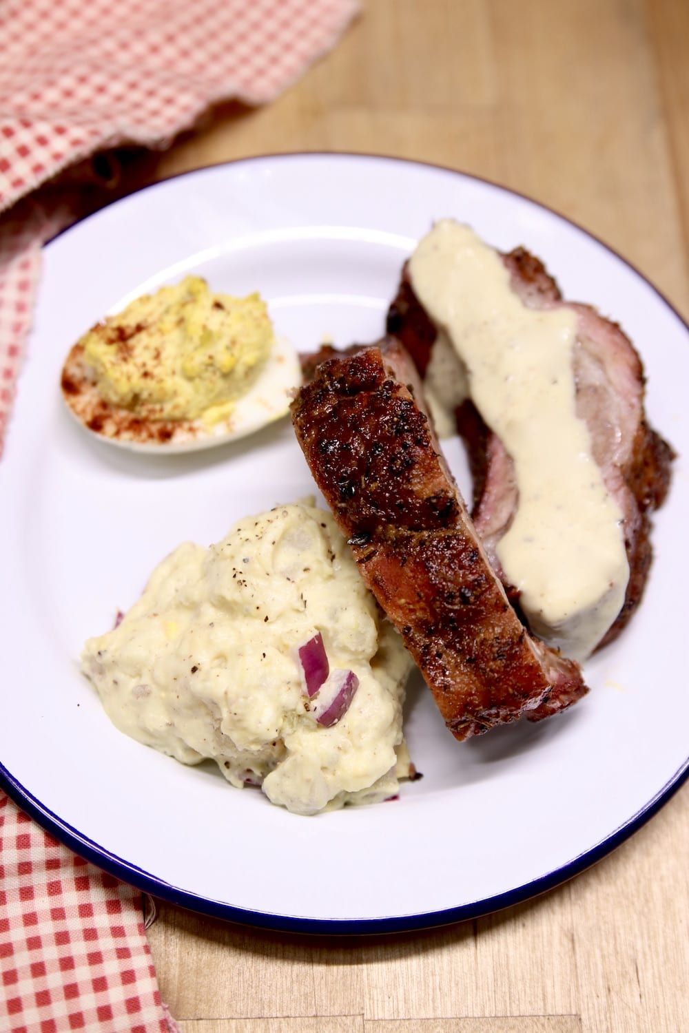 plate of 2 baby back ribs with white bbq sauce, potato salad, deviled egg