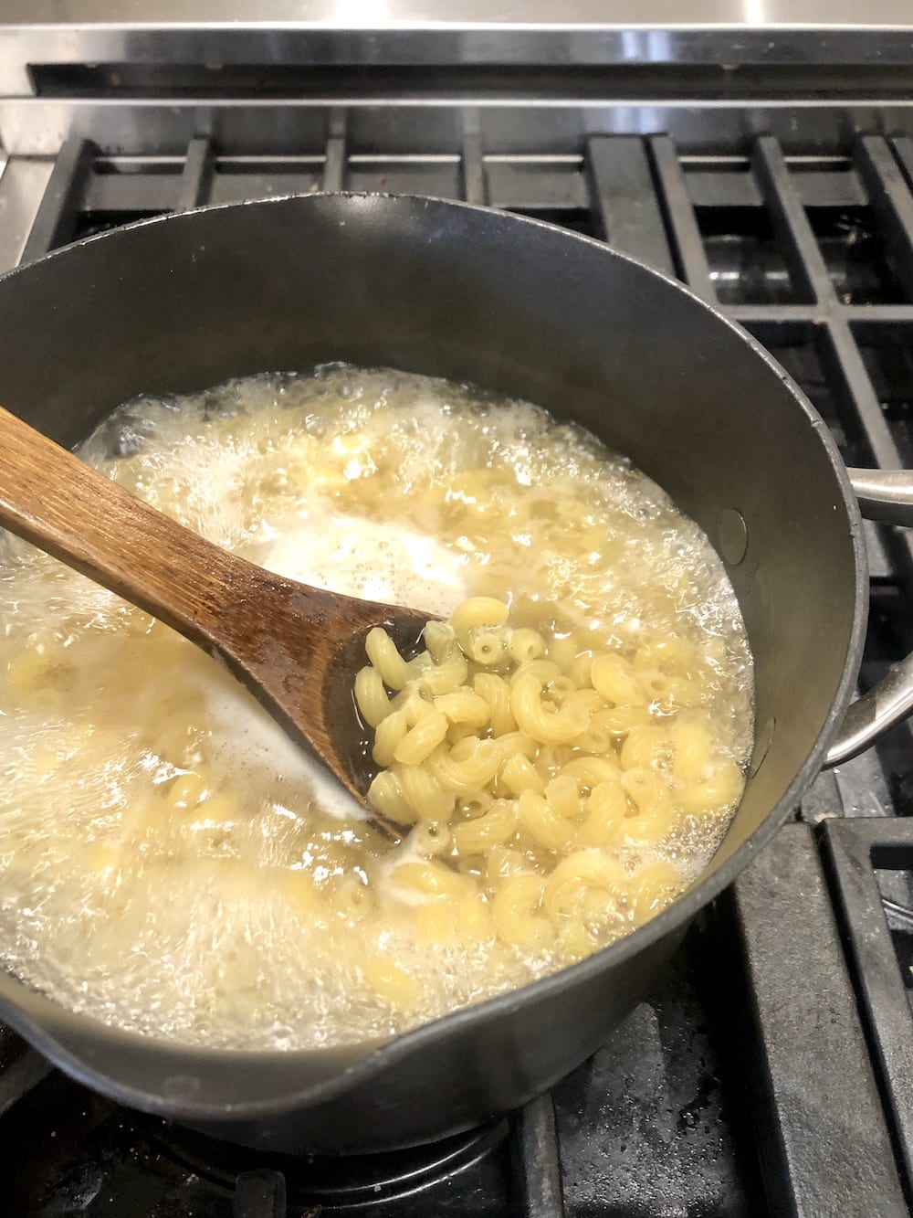 pan of boiling macaroni with a wood spoon