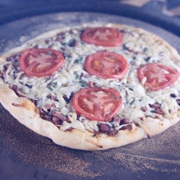 Brisket pizza topped with tomato slices on a pizza stone - grilling