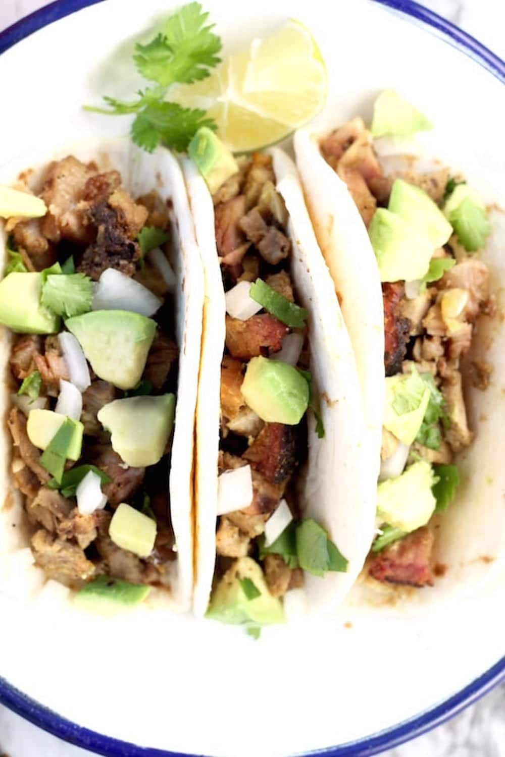 closeup of plated pork tacos with onions and avocado