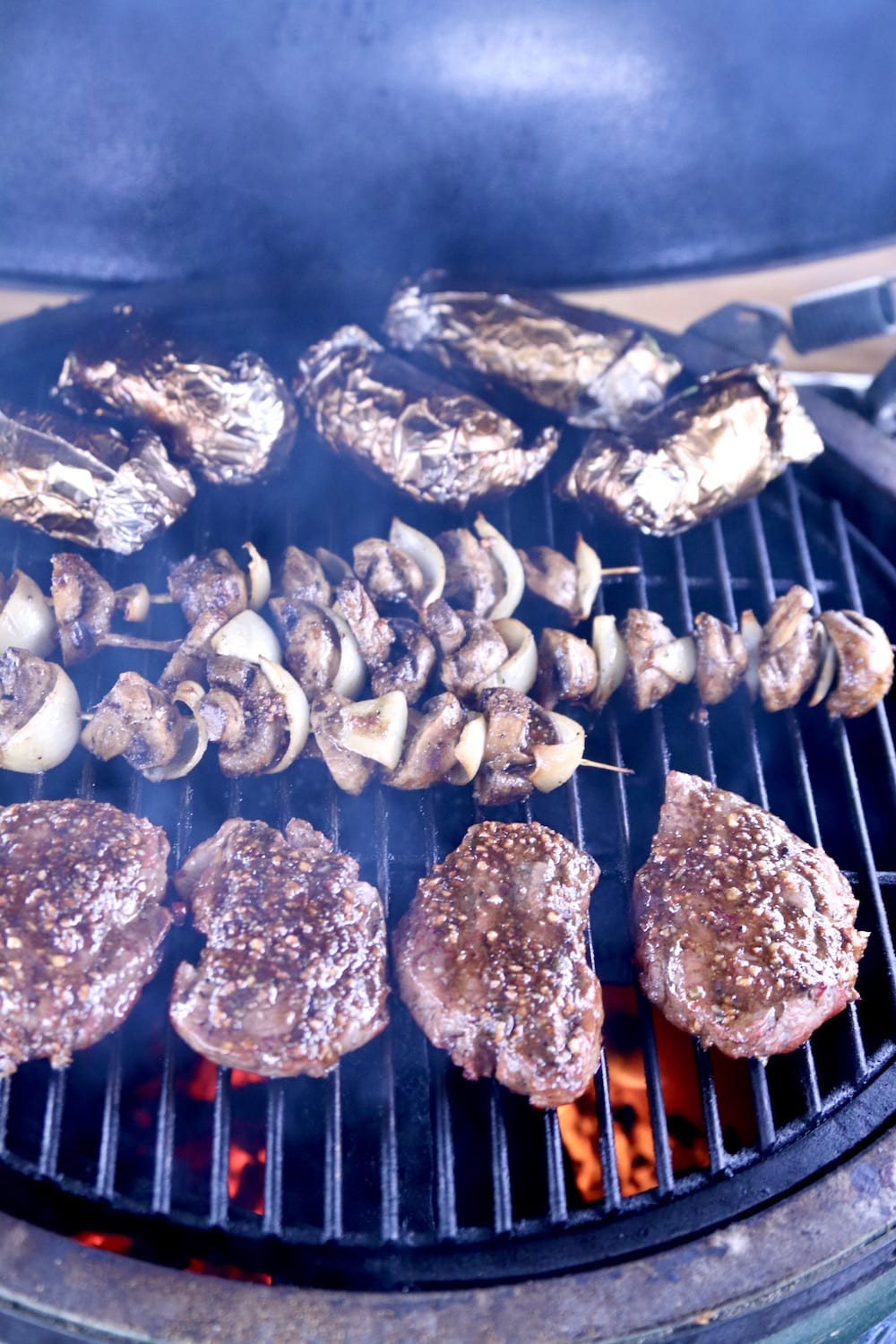 steaks, with mushrooms and baked potatoes on a grill