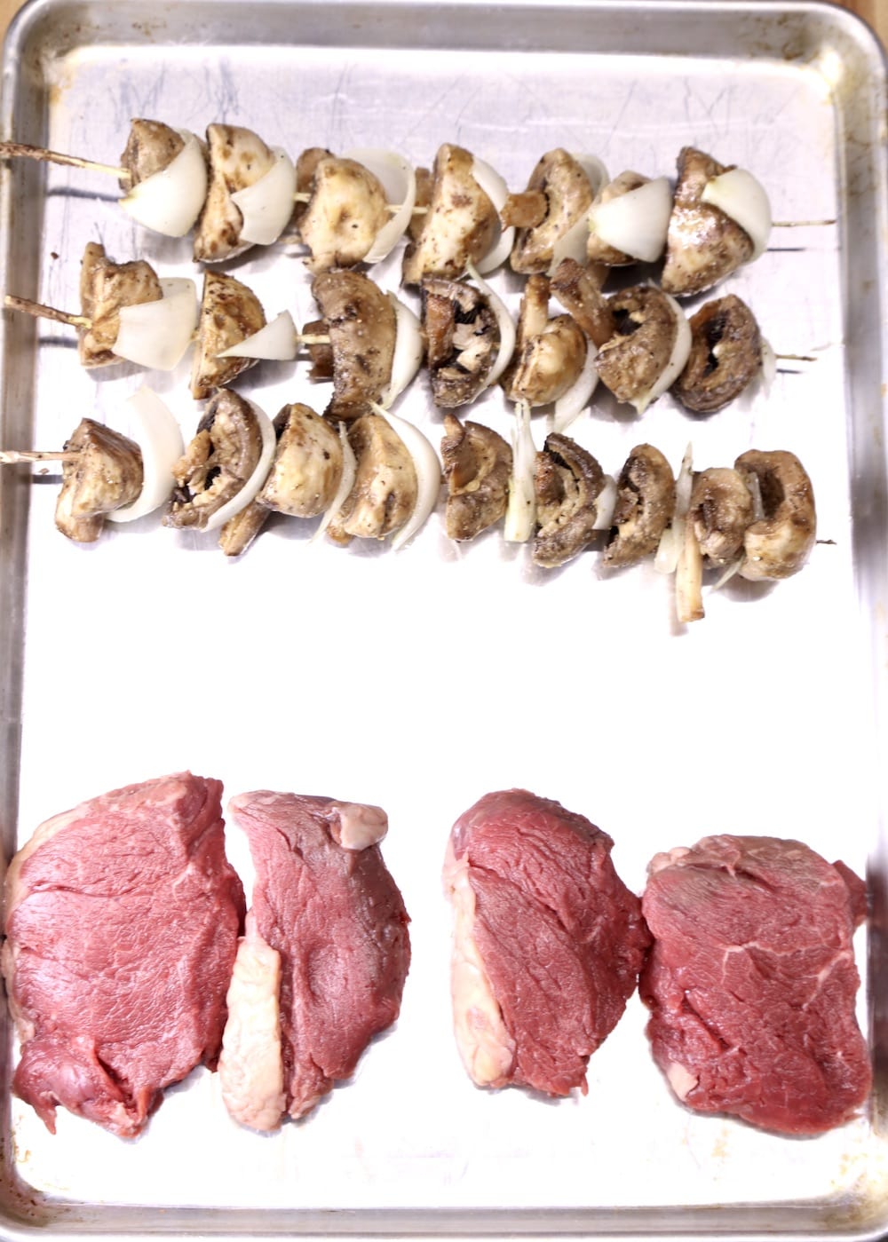 mushroom and onion skewers with 4 tenderloin steaks on pan