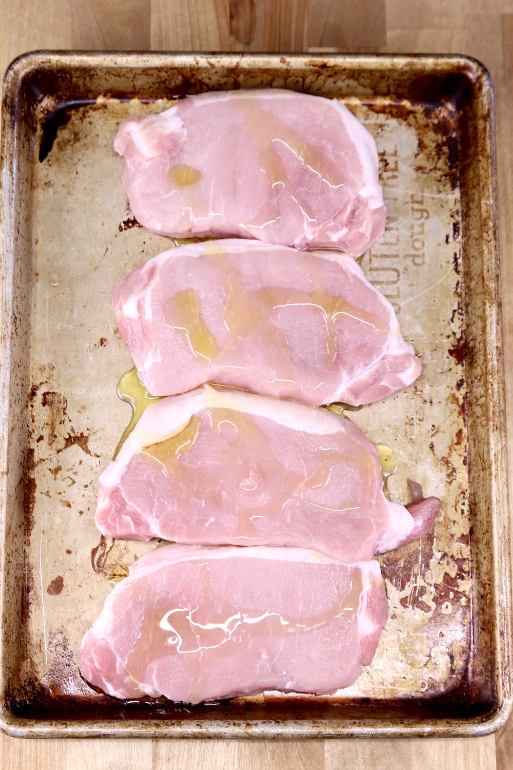 4 pork chops on a baking sheet drizzled with olive oil