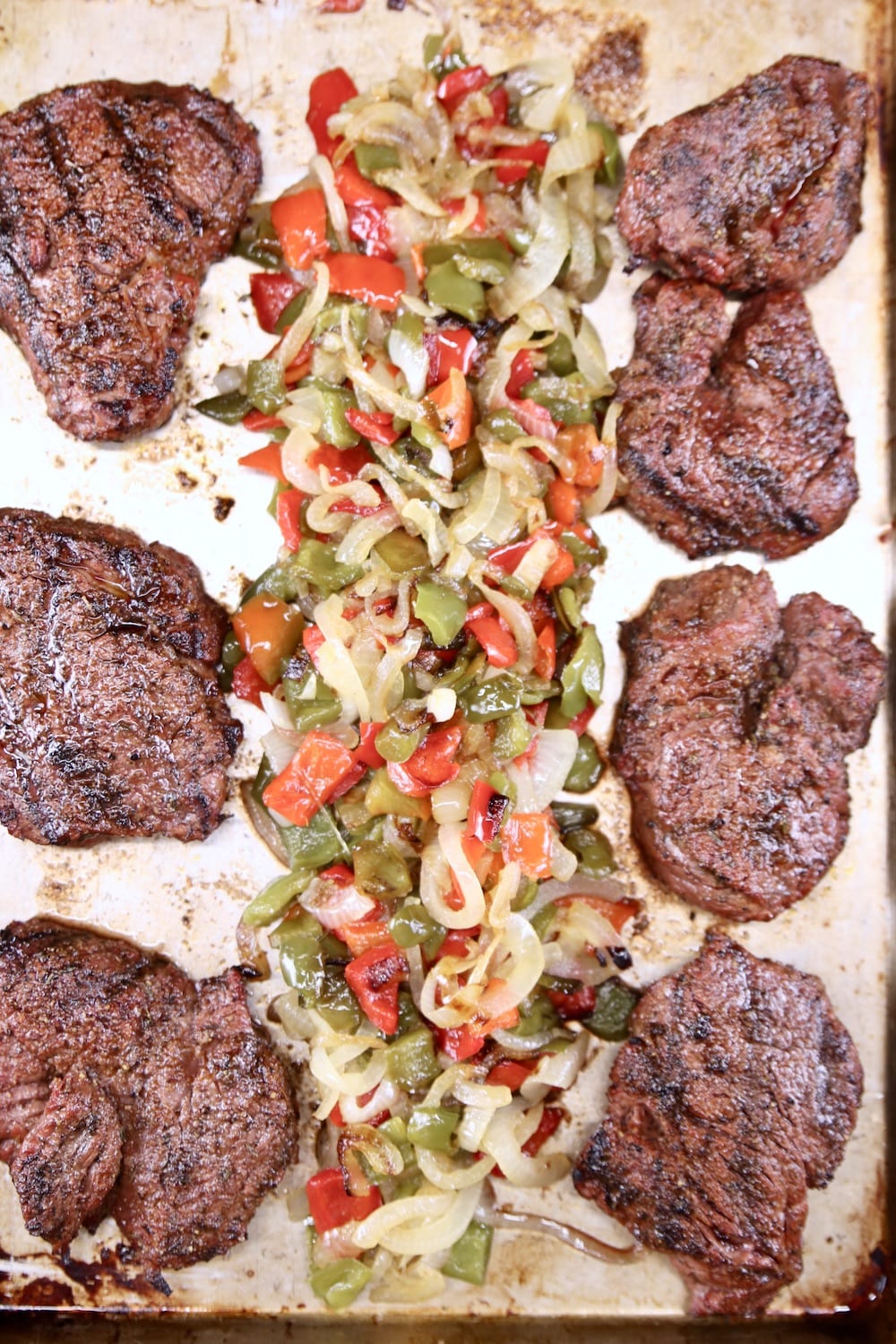 grilled filet mignon steaks on a sheet pan with peppers and onions down the center