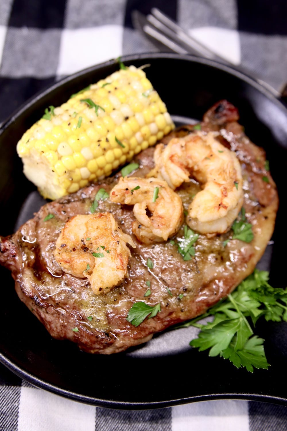 black serving skillet with ribeye steak topped with shrimp. Served with corn on the cob
