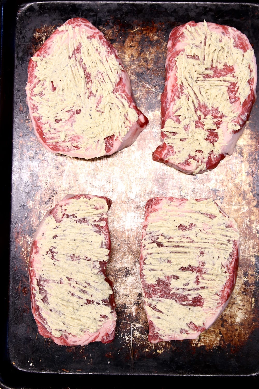 4 ribeye steaks coated with seasoned butter on a sheet pan