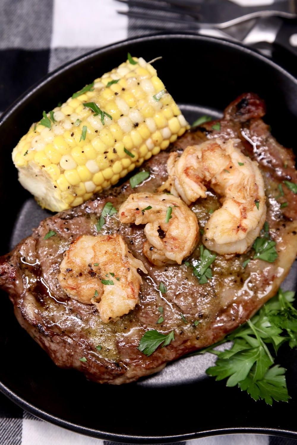serving skillet with grilled steak, 3 shrimp, corn on the cob
