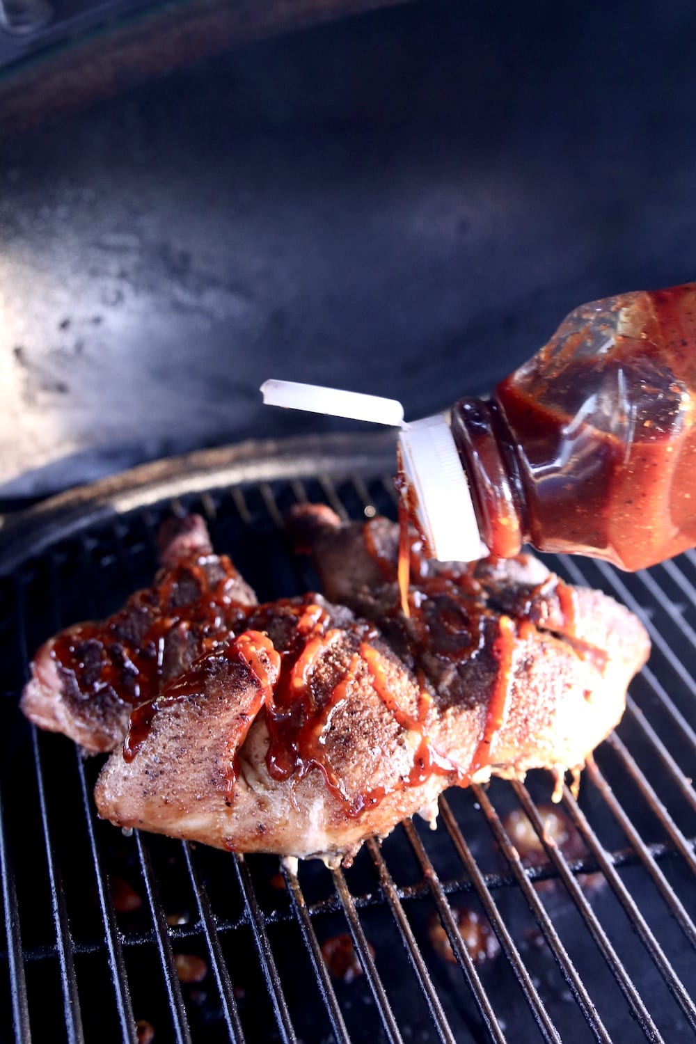 Pouring BBQ Sauce on chicken on the grill