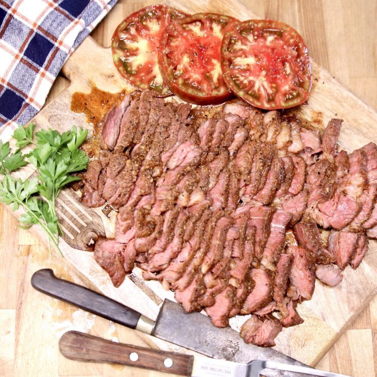 sliced roast beef on a cutting board with sliced tomatoes