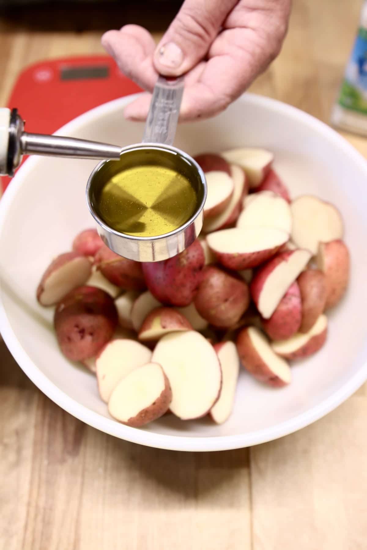 potatoes in a bowl, drizzling with olive oil