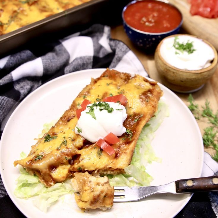 Chicken Enchiladas on a plate with sour cream and tomatoes