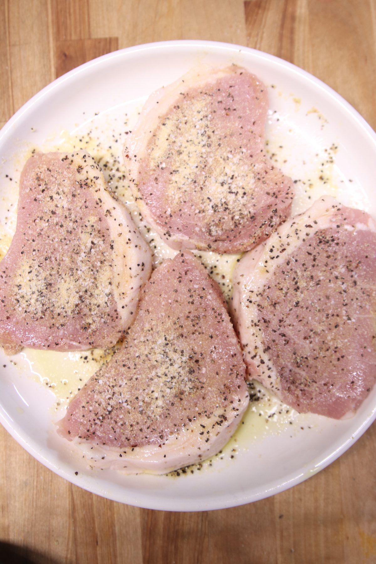 seasoned raw pork chops on a white plate