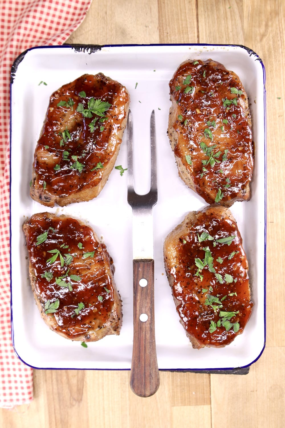 4 BBQ pork chops on a white tray with meat fork in center