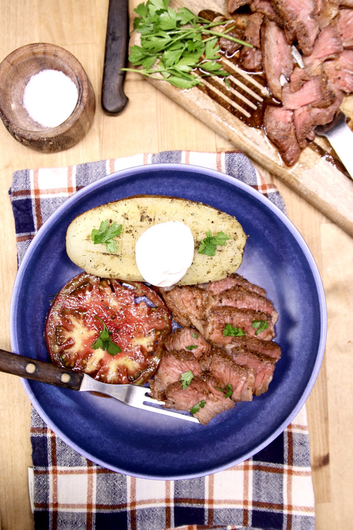 bowl of sliced roast beef, baked potato and sliced tomatoes