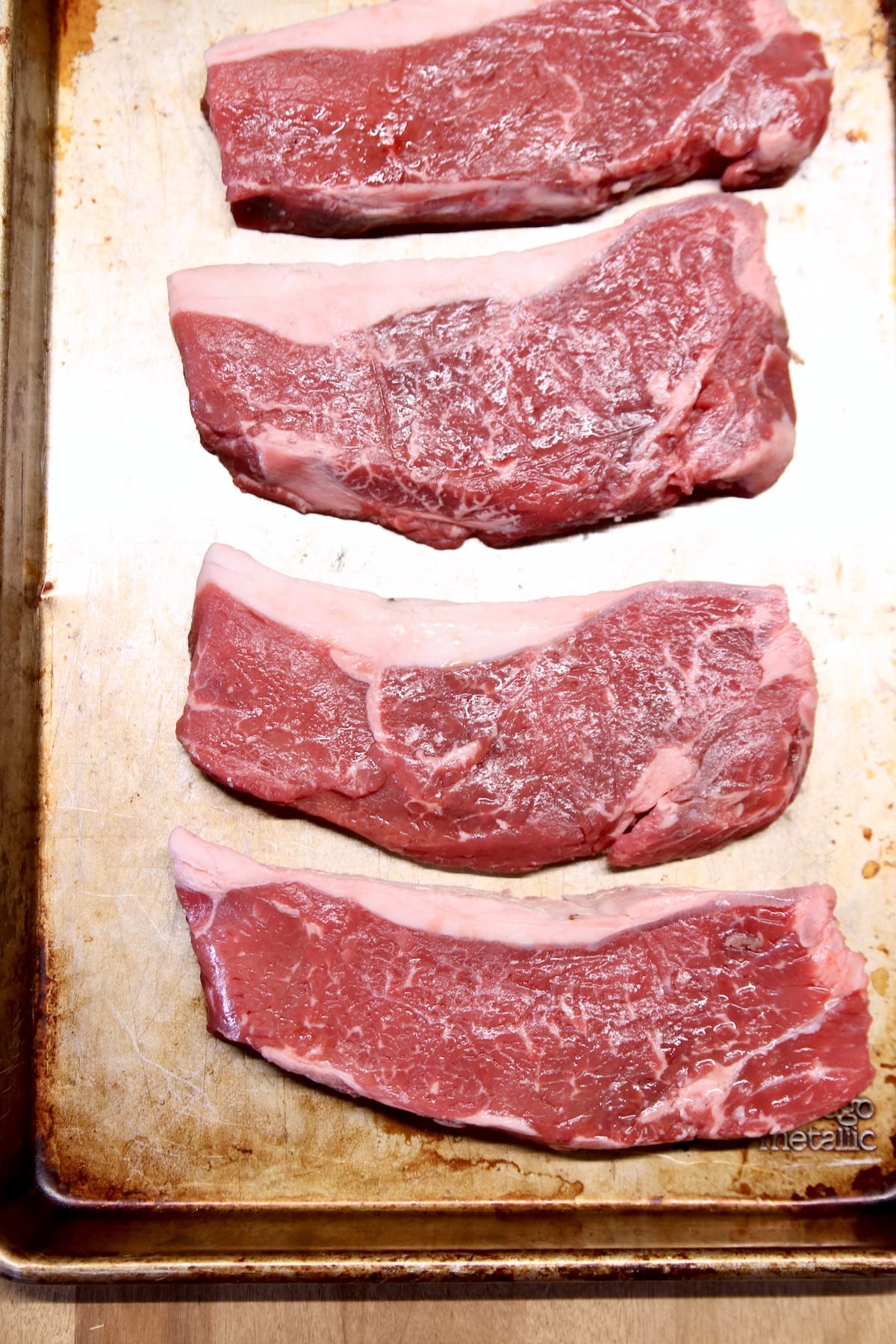 4 raw strip steaks on a sheet pan