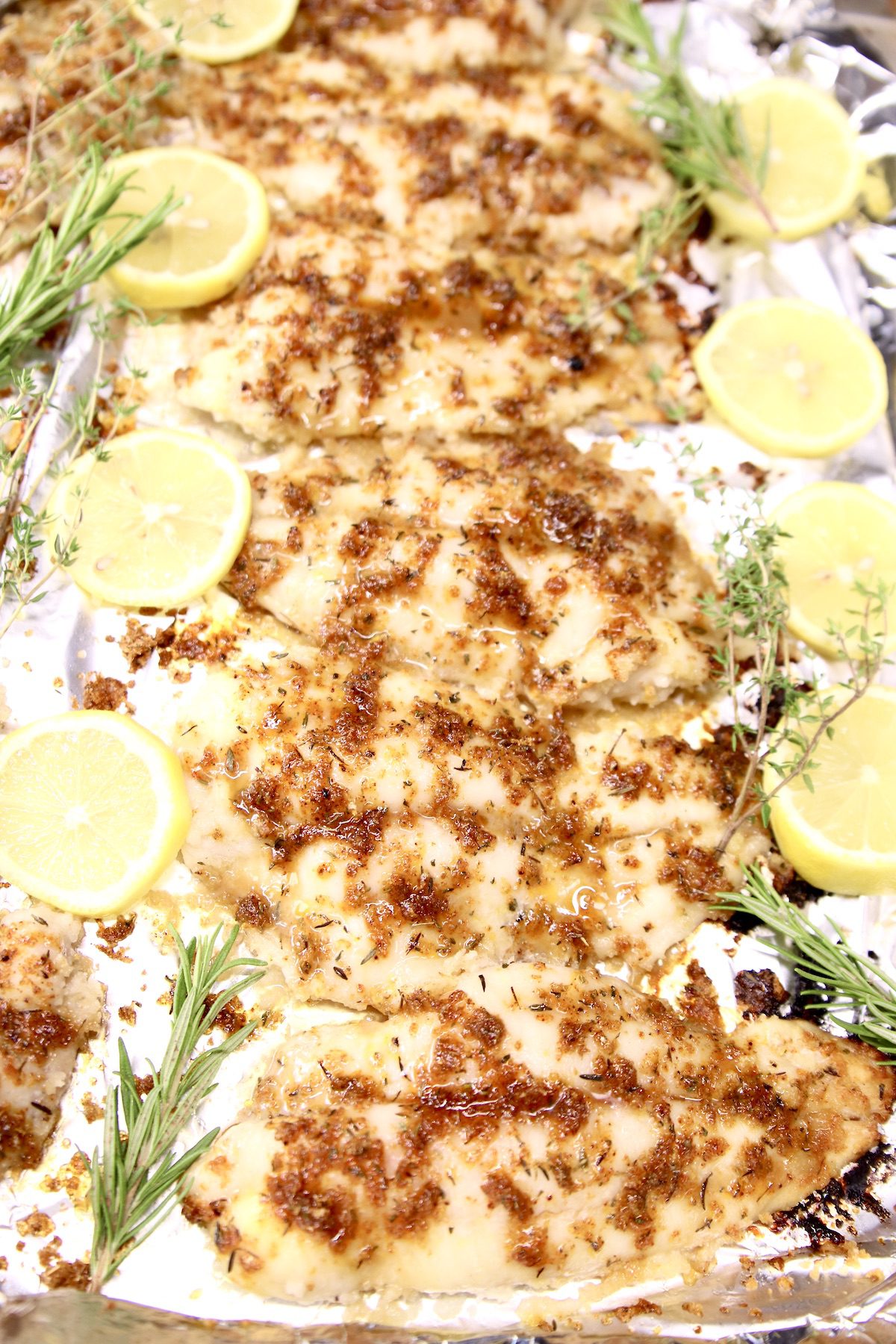 foil lined pan with grilled lemon catfish - lemon and herb garnishes
