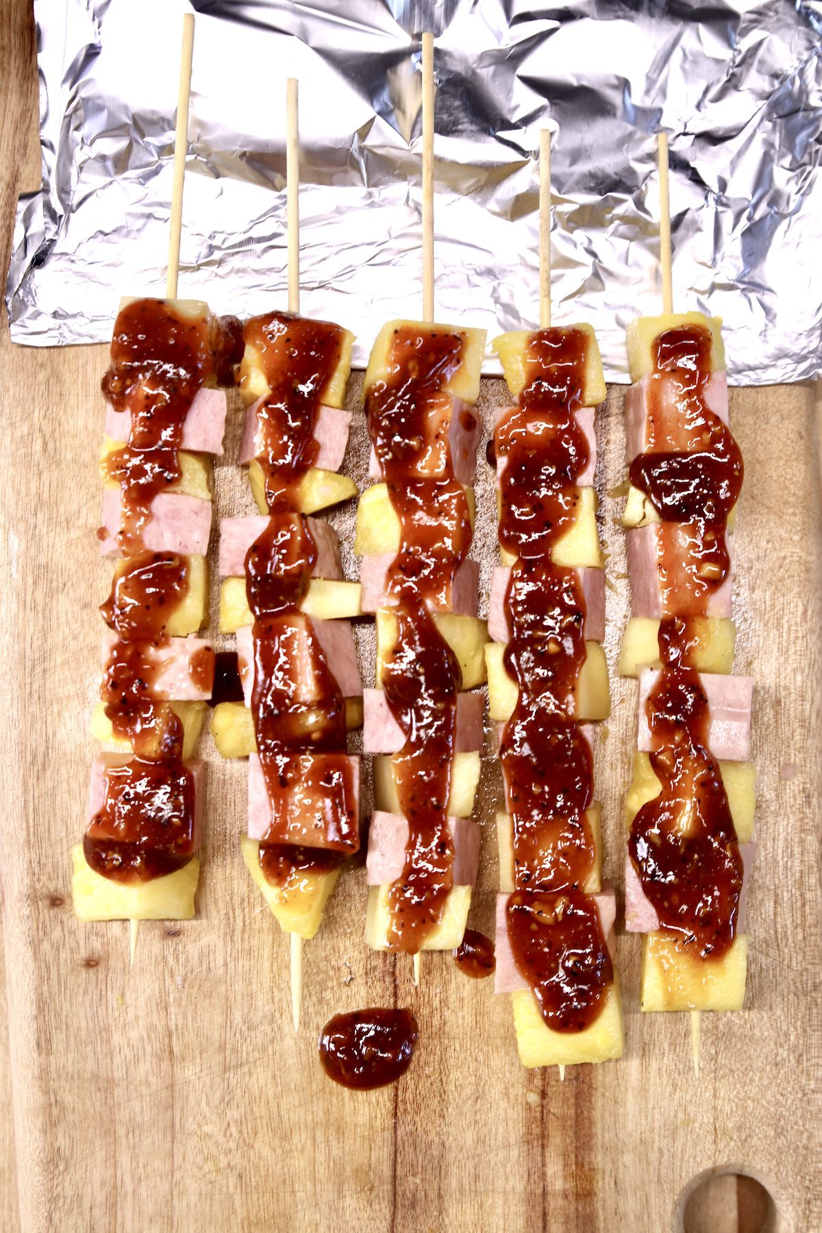 spam and pineapple kabobs with bbq sauce with foil under skewers for grilling
