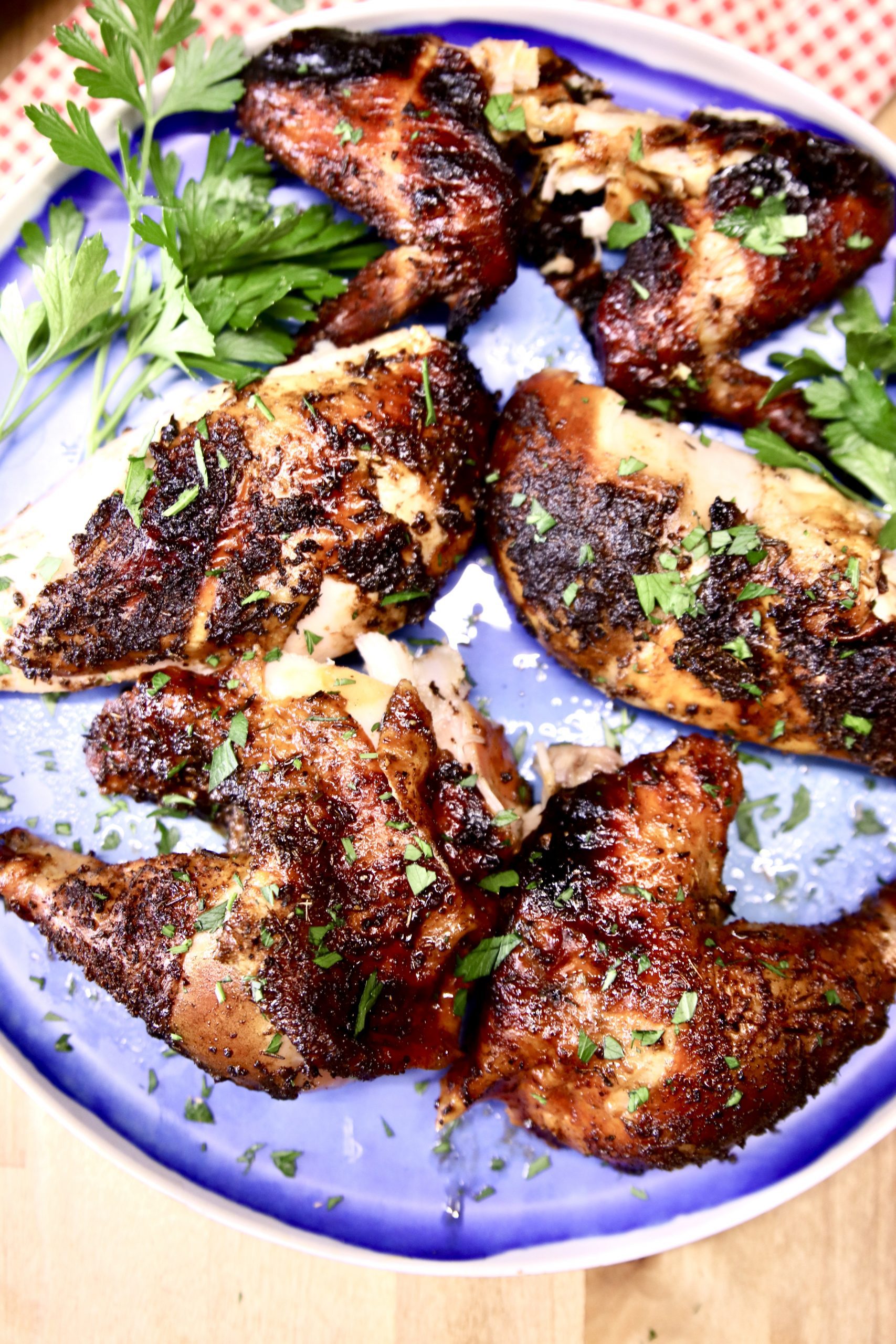 cut up grilled chicken on a blue plate with parsley garnish