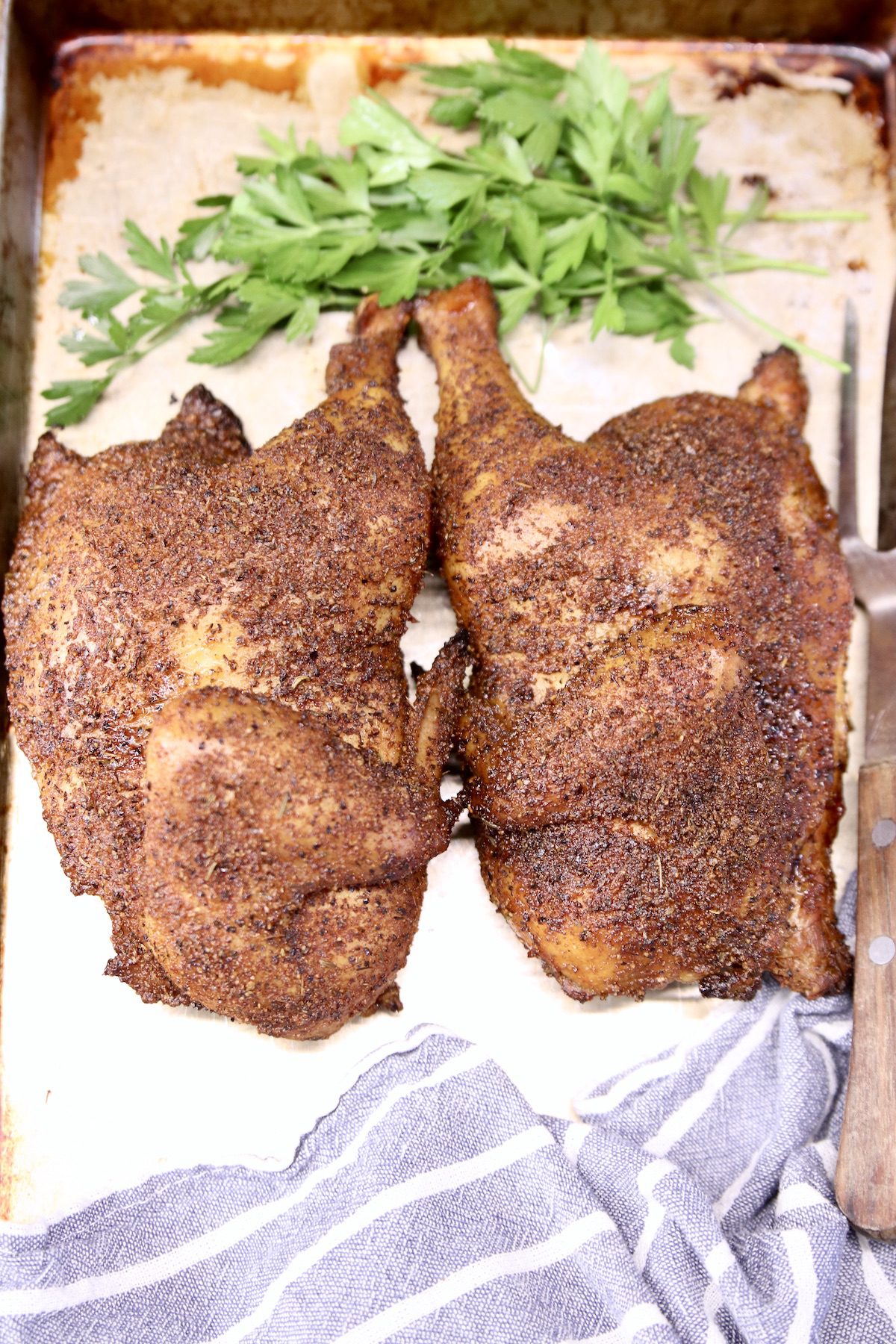 half chickens grilled with dry rub on a sheet pan with parsley