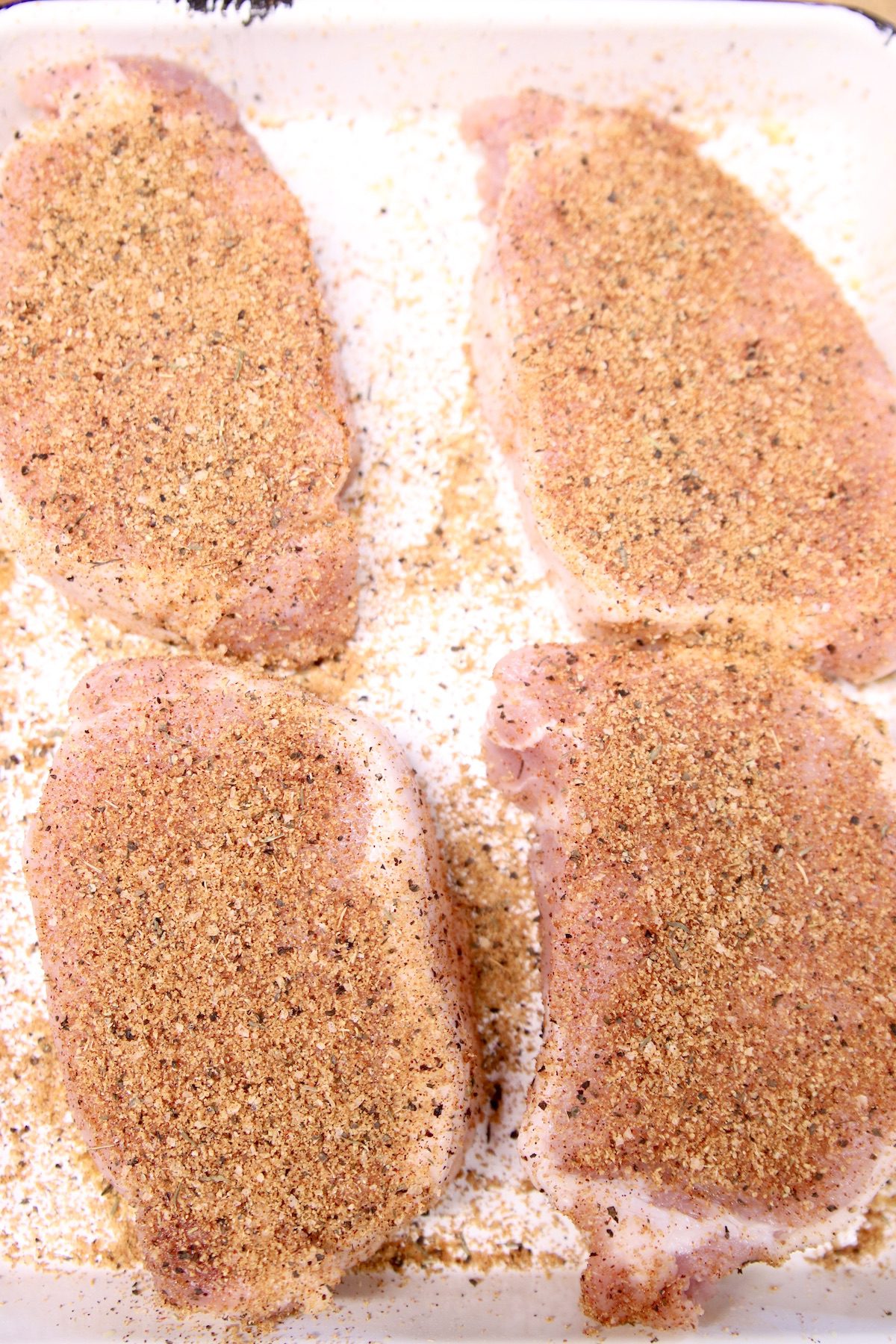 4 boneless pork chops on a sheet pan with dry rub seasoning - raw