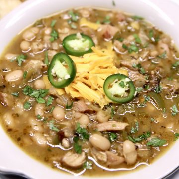 bowl of white bean chicken chili garnished with shredded cheddar and 3 slices of jalapeno