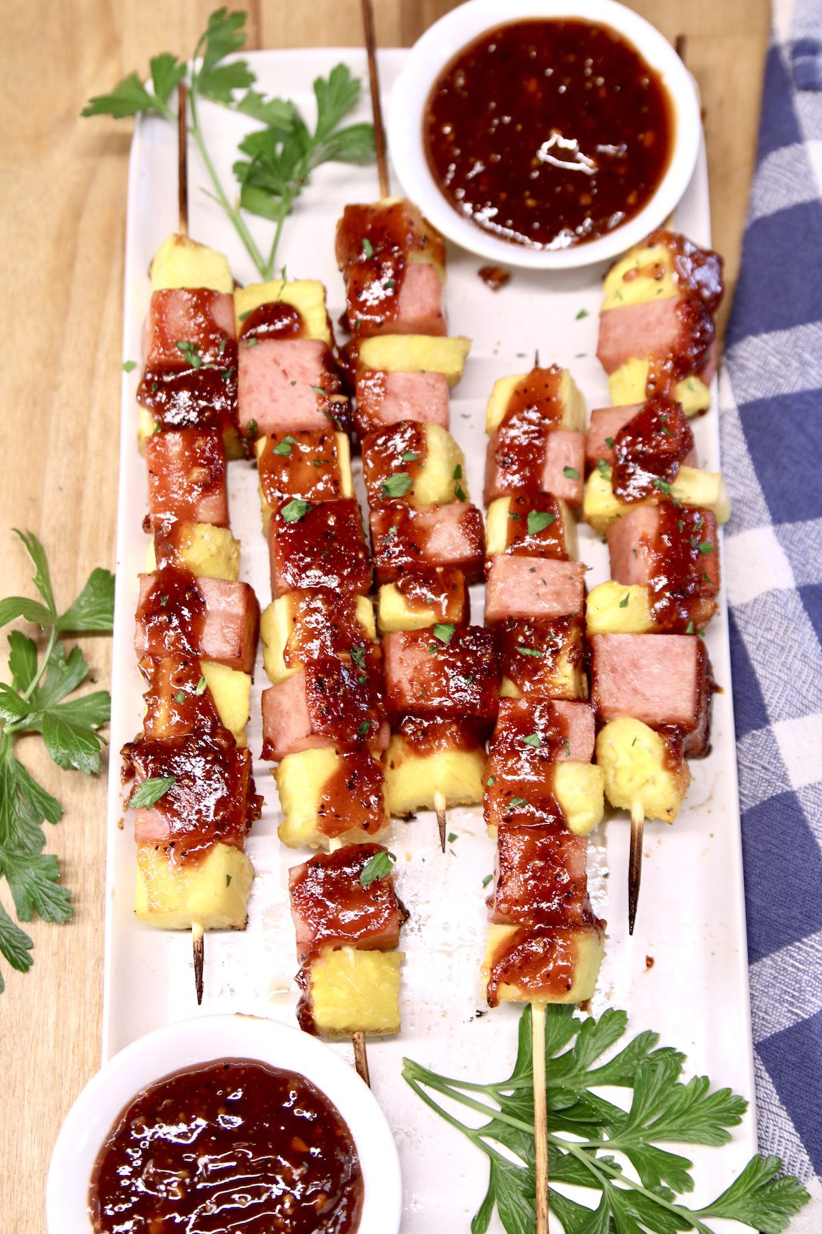 platter with spam and pineapple kabobs - 2 small bowls of bbq sauce, parsley garnish