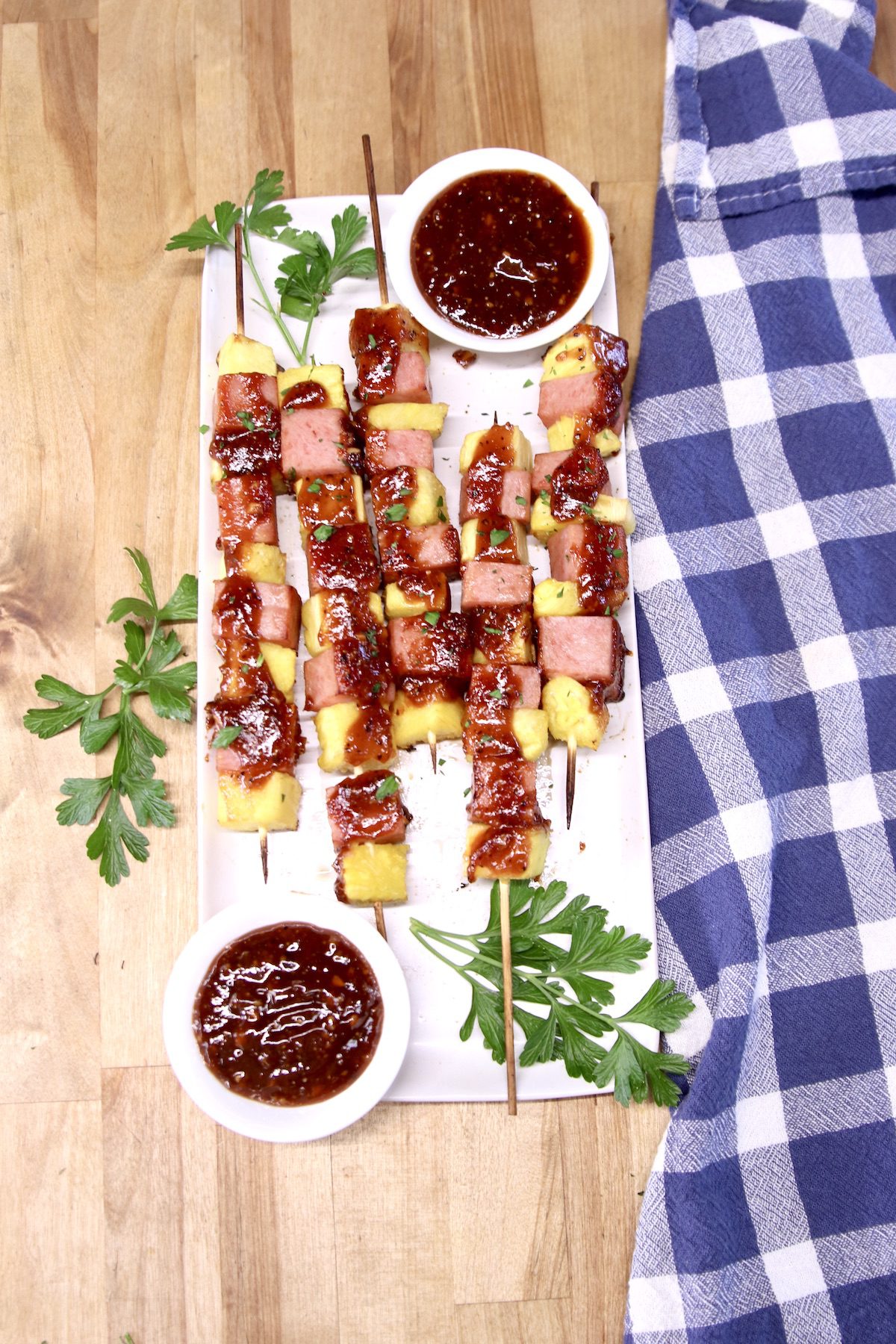 overhead of platter of kabobs with spam and pineapple, bowls of bbq sauce