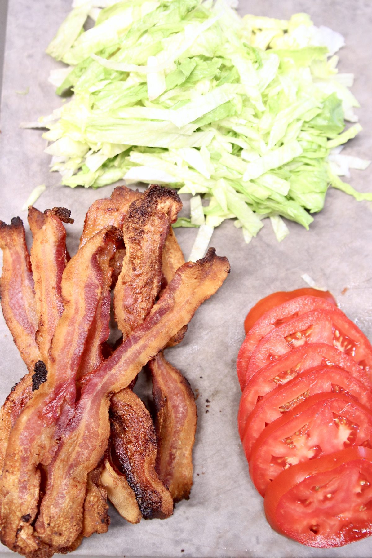 bacon slices, tomato slices, shredded lettuce on a cutting board