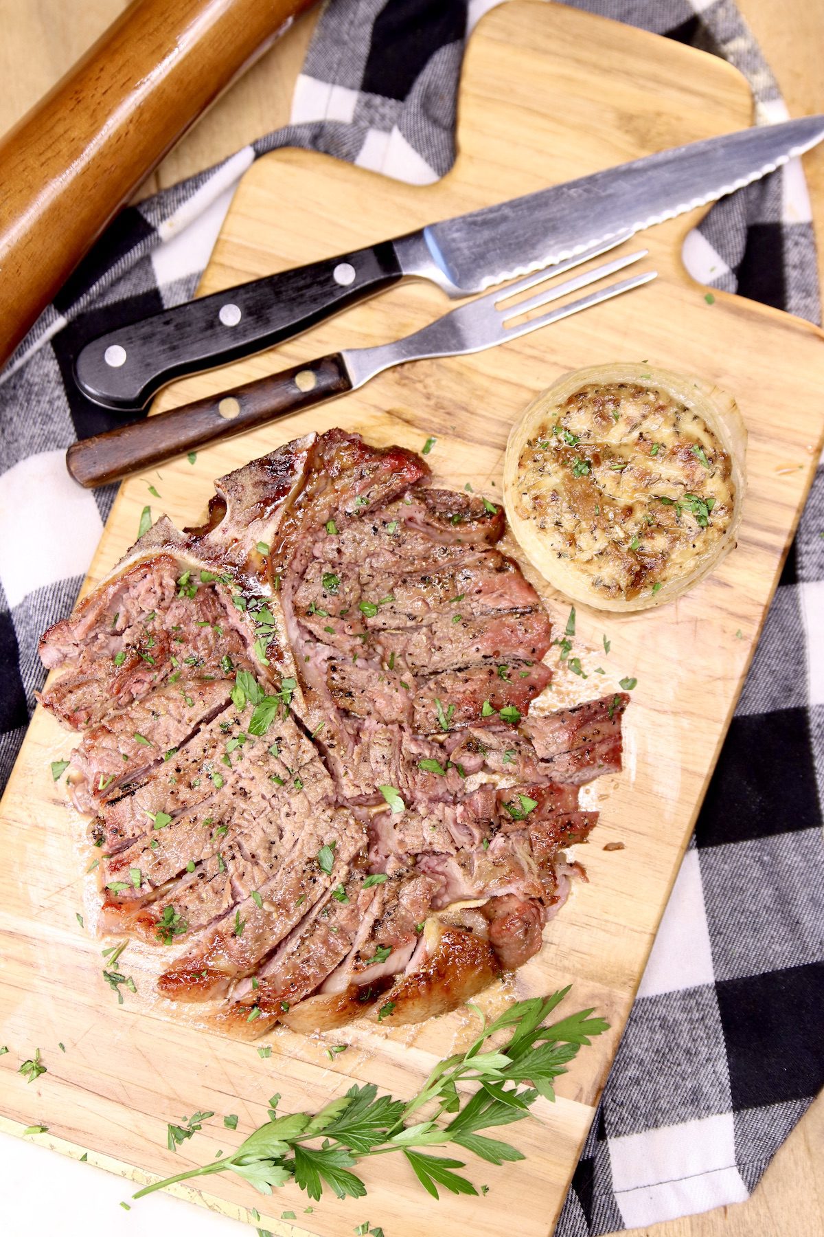 sliced t-bone steak on a board, knife and meat fork