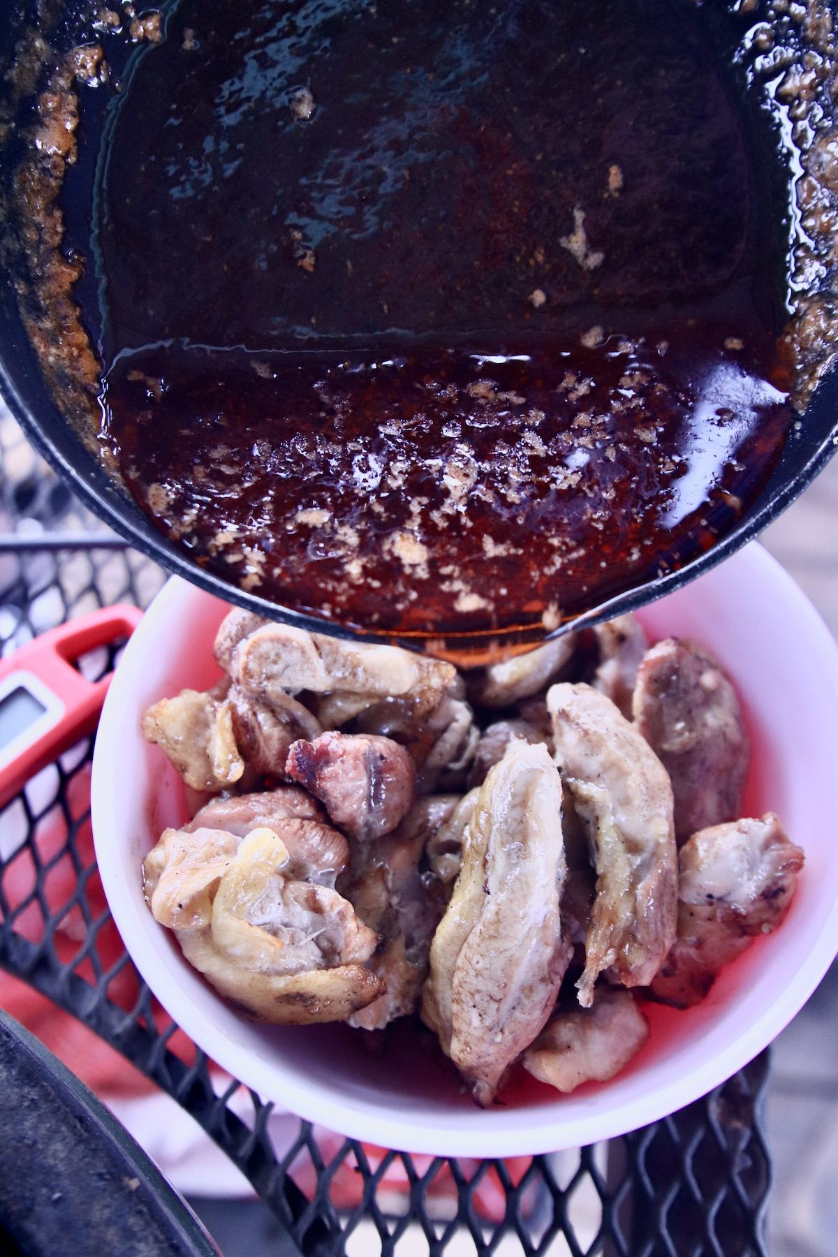 pouring hot honey sauce over wings in a bowl