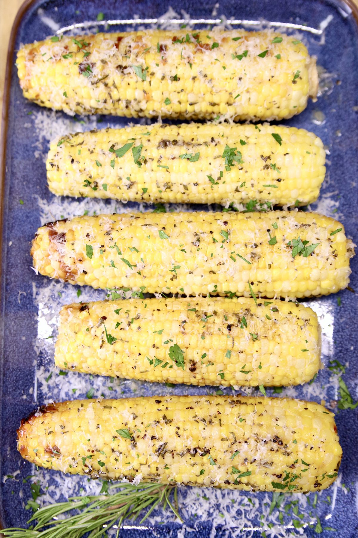 parmesan corn on the cob on a blue platter, herb garnish