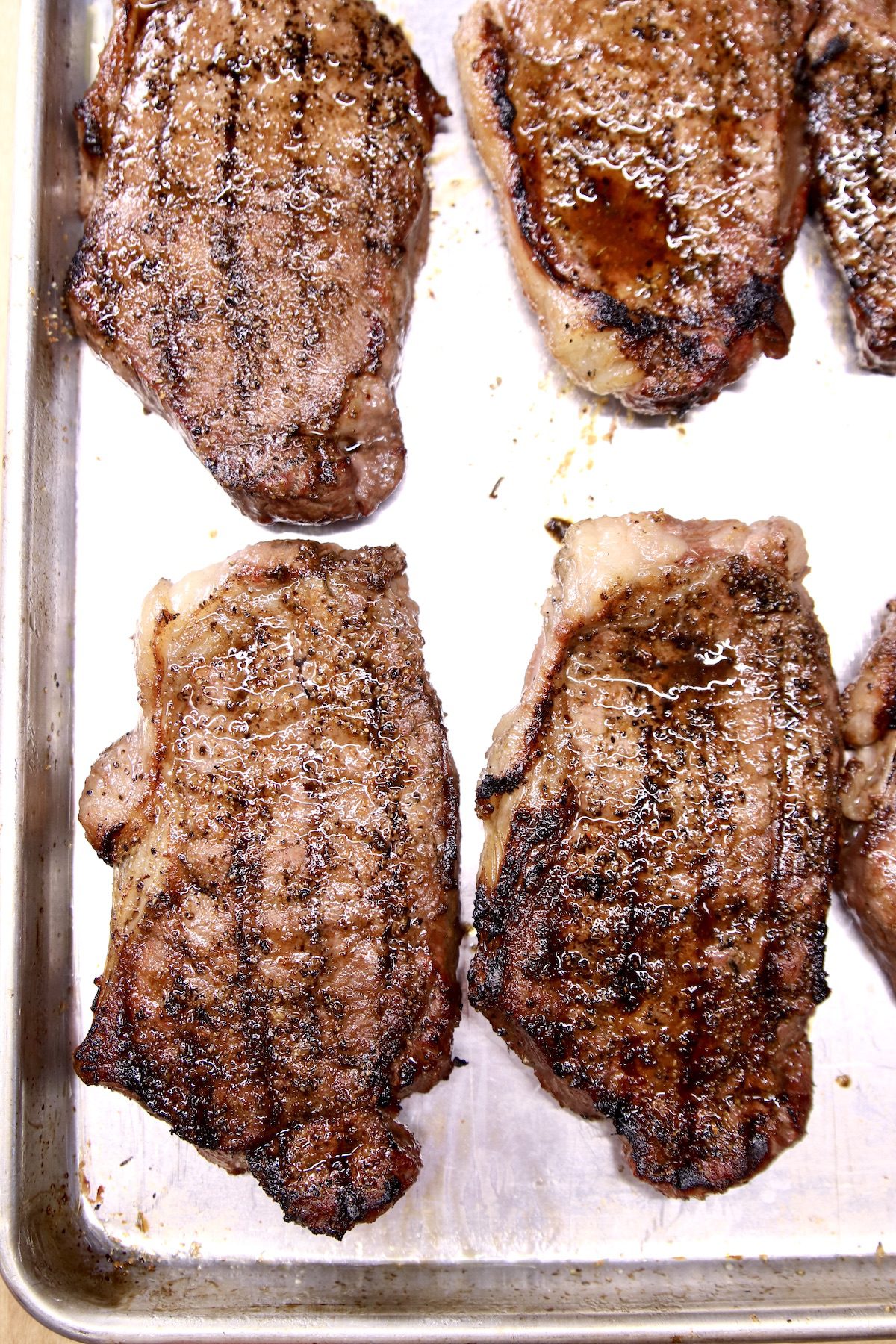 grilled strip steaks resting on a sheet pan