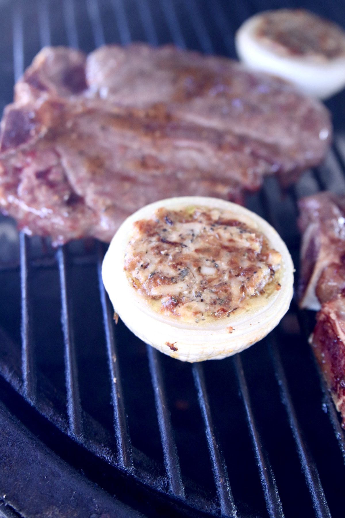 grilled onions stuffed with cheese on a grill with steaks