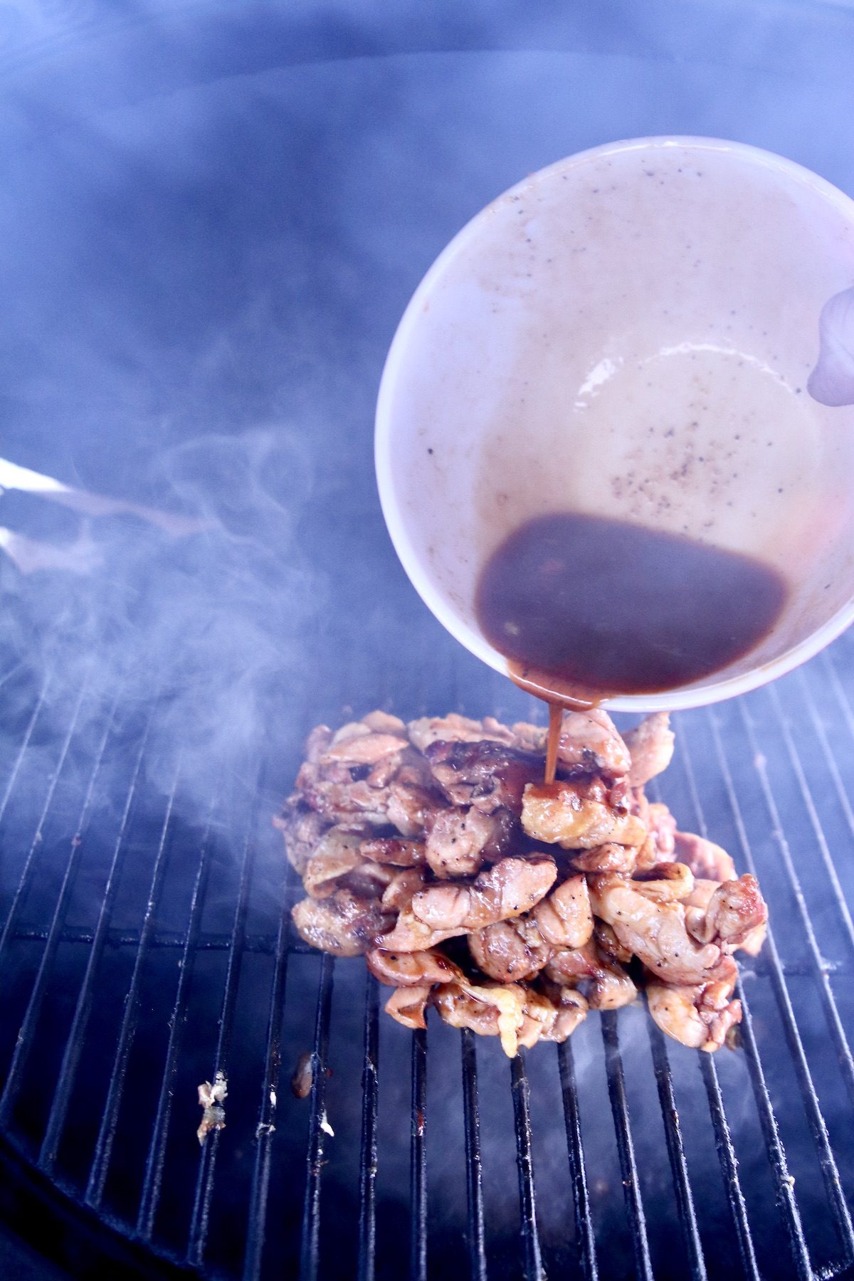 pouring sauce over chicken wings on a grill