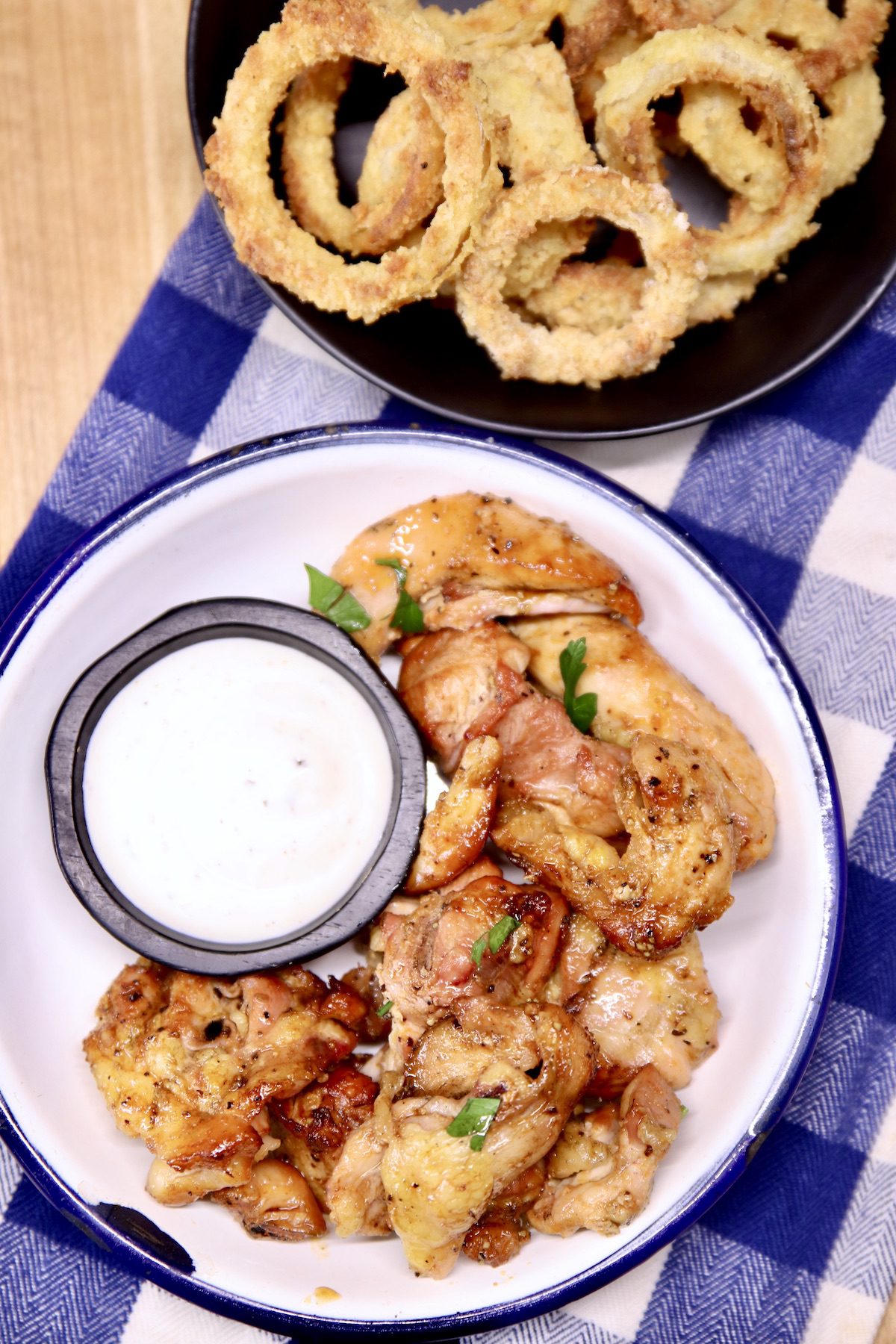 hot honey chicken wings with ranch dressing in a bowl - bowl of onion rings to the side