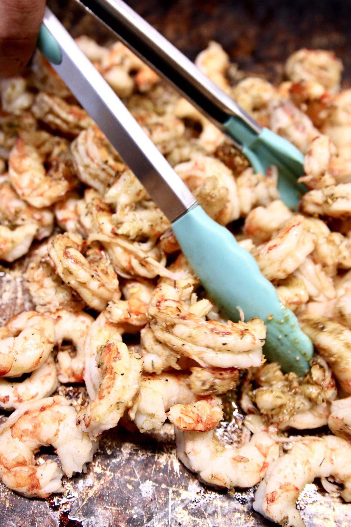 tongs tossing shrimp with garlic butter on a sheet pan