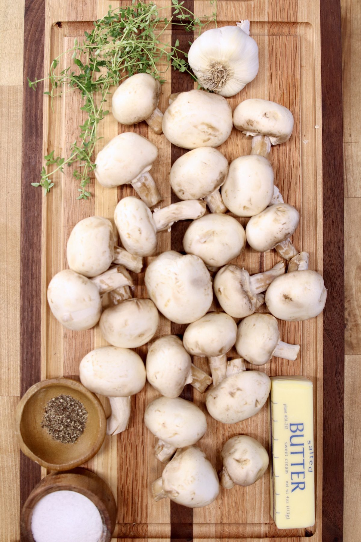 mushrooms sliced in half on a cutting board with stick of butter, bowls of salt & pepper + fresh thyme