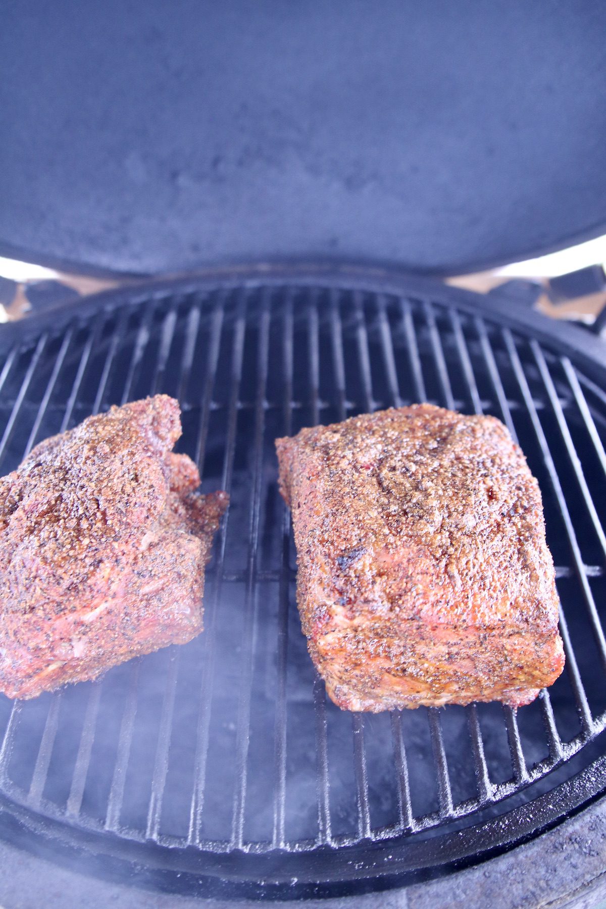 2 pork shoulders on a grill with dry rub seasoning