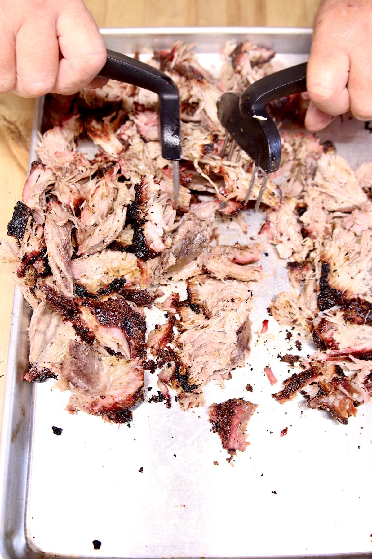 using meat claws to shred pork butt on a sheet pan