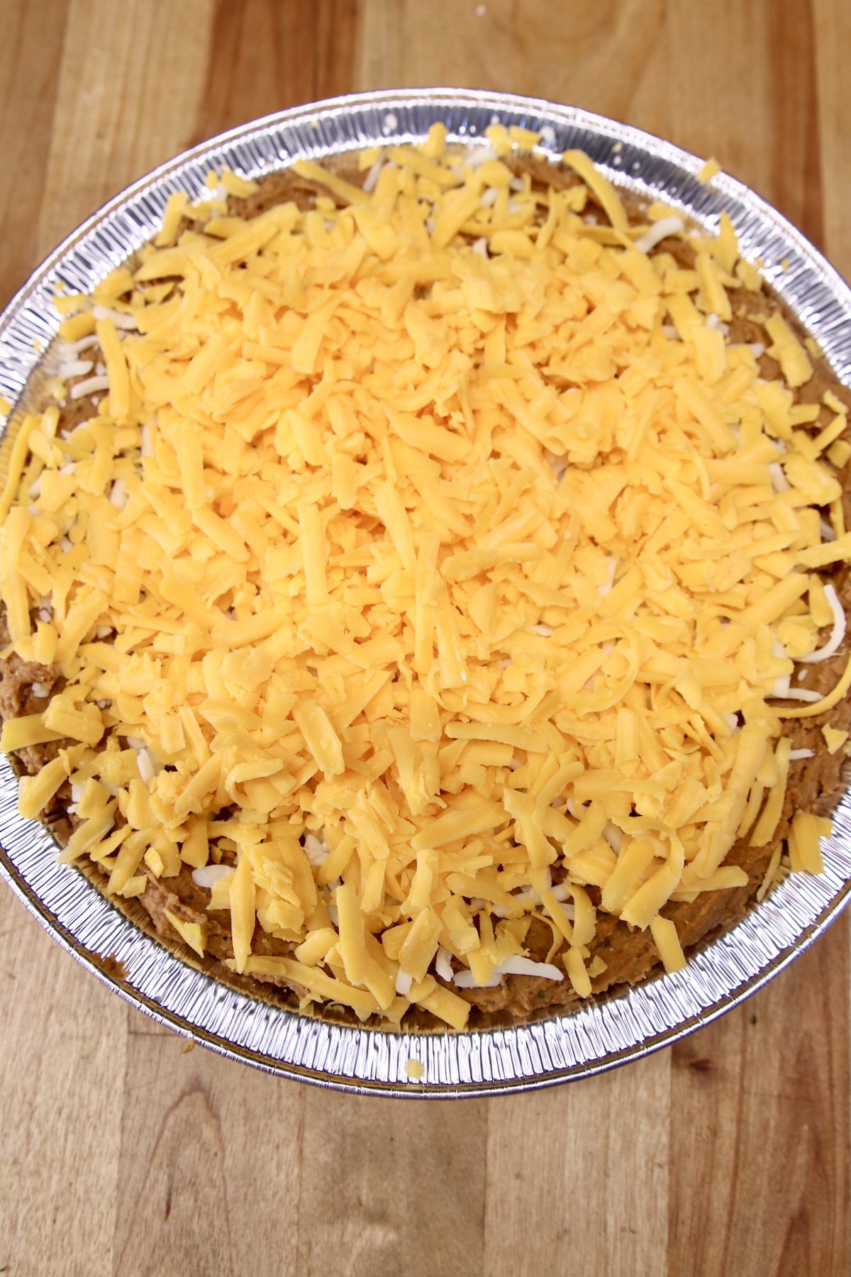 foil pie plate with bean dip topped with shredded cheddar cheese