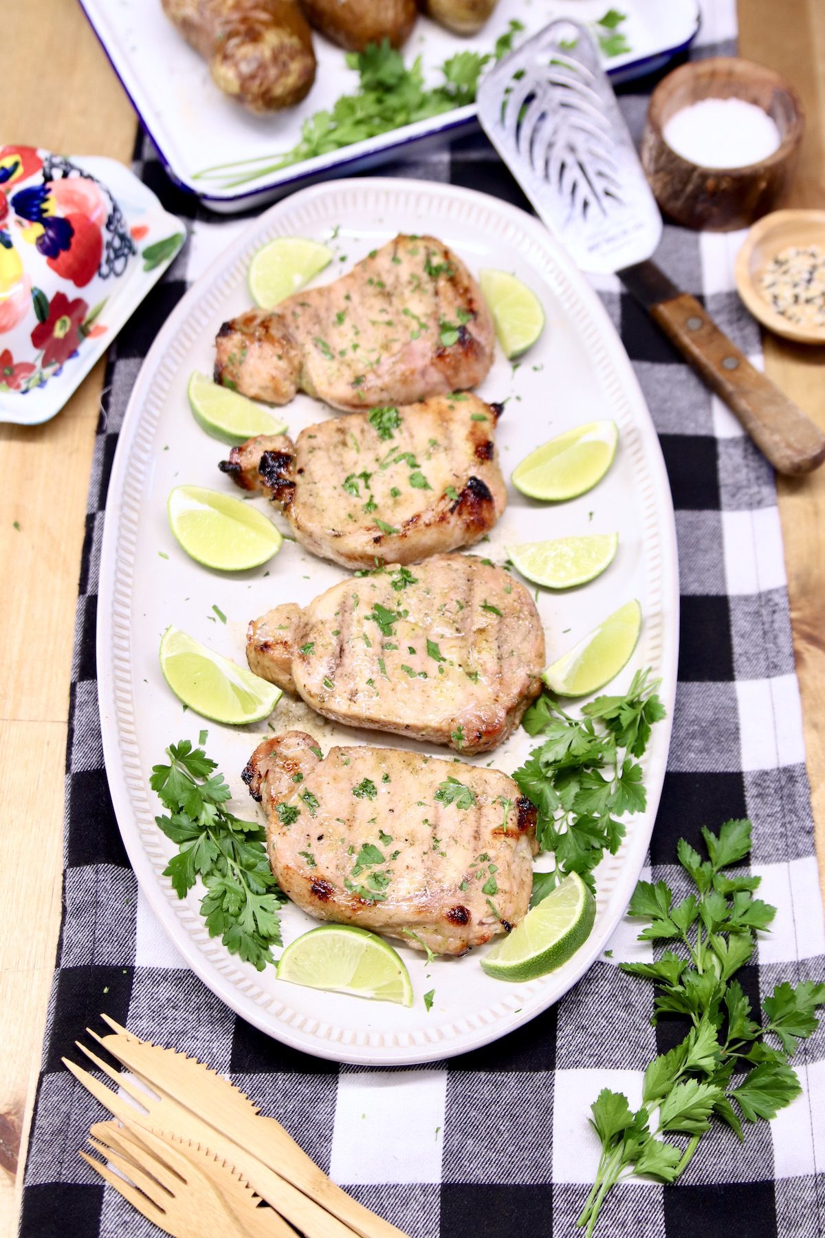 platter of pork chops with limes and cilantro on a black and white checked table runner
