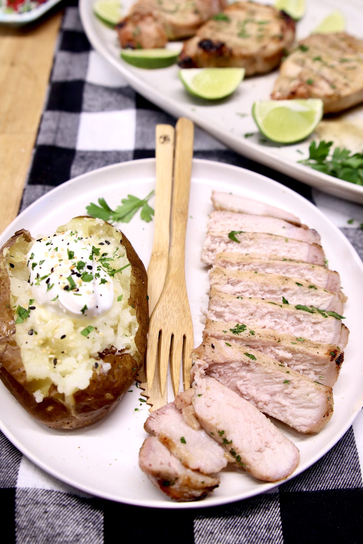 Grilled pork chops sliced on a plate with a baked potato, fork & knife