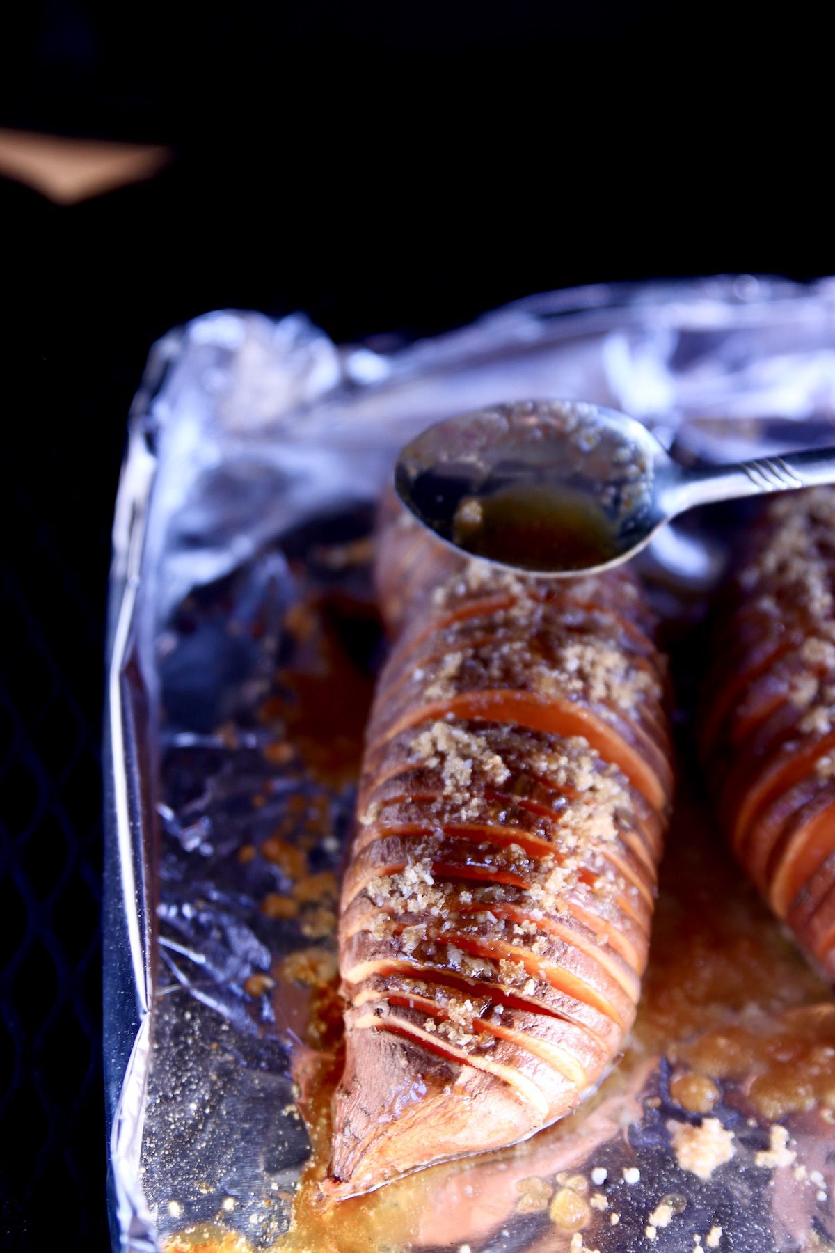 spooning butter mixture over hasselback sweet potatoes on the grill